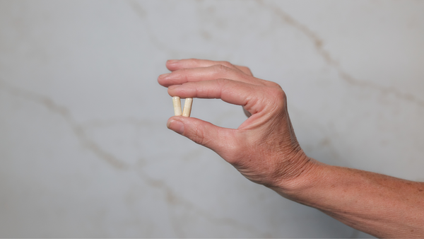 A hand holding two Neuralli Mood cortisol reducing probiotic capsules against a marble-patterned wall