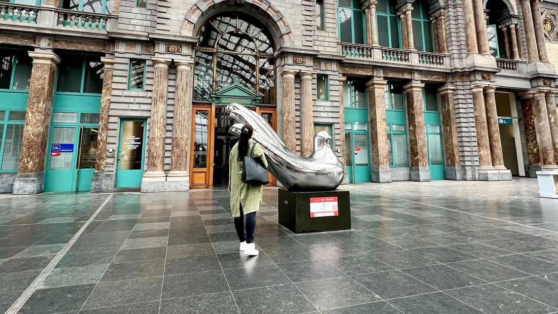 Autistic woman standing in front of a large bird sculpture outside a European train station