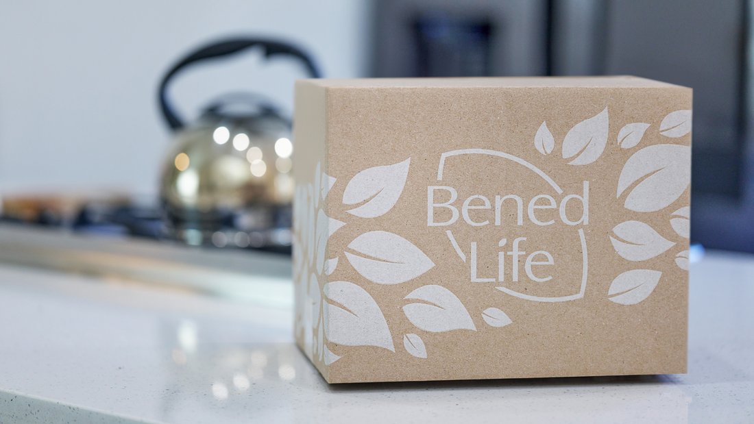 A Bened Life shipping box sits on a white countertop. A stove with a kettle is in the background.