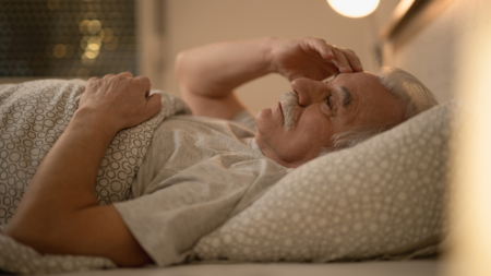 An elderly man lays awake in his bed