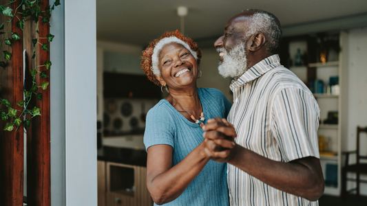 A senior couple dances, smiling, in their living room with the kitchen in the background.