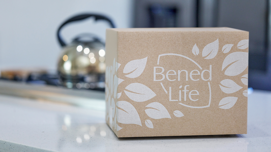 A Bened Life shipping box sits on a white countertop. A stove with a kettle is in the background.