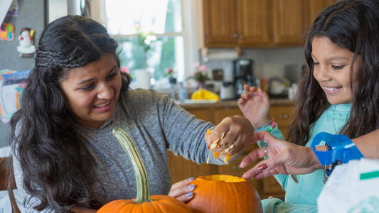 An Autistic girl removes the innards from a pumpkin to make a jack o lantern as her little sister smiles