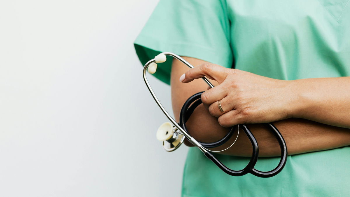 Doctor in scrubs, arms folded, holding a stethoscope