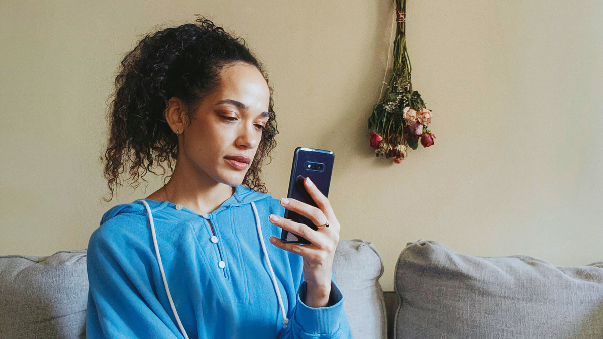 A woman in a blue hoodie looks at her phone. 