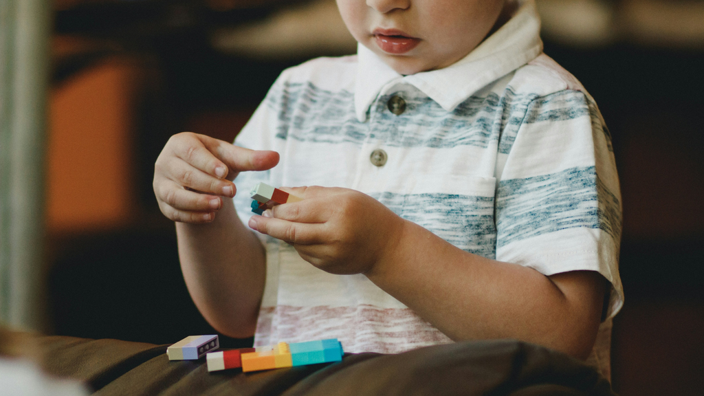 A small child in a striped shirt plays with multicolored Lego blocks