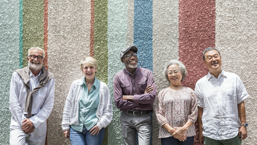 Five seniors stand in a line together, smiling, against a multicolored wall