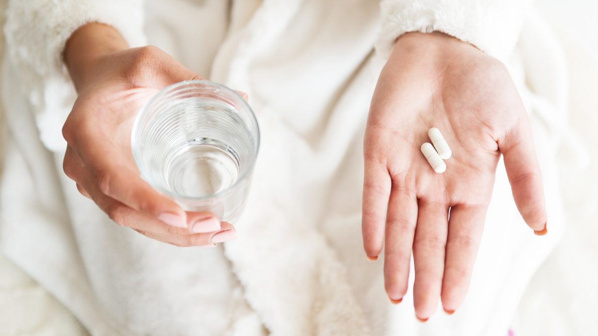 Woman's hands, one holding a glass of water, one with two capsules of Neuralli