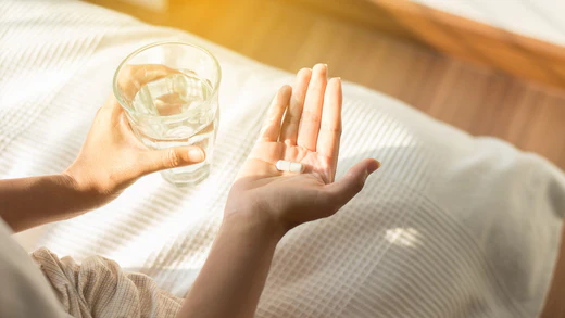 tangan seorang wanita, memegang segelas air dan kapsul probiotik, mengilustrasikan probiotik untuk mendukung kesehatan mental