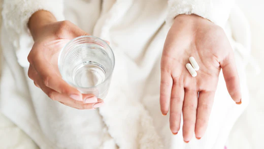 Woman's hands, one holding a glass of water, one with two capsules of Neuralli